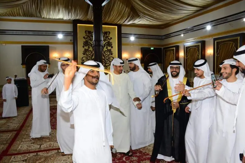 Guests dancing Ayala with canes at an Emirati wedding celebration in a majlis hall